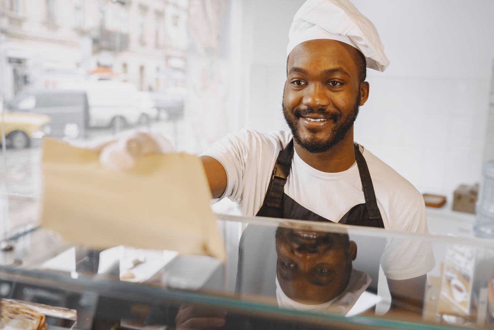 A café employee handing a bakery paper bag to a customer at the counter