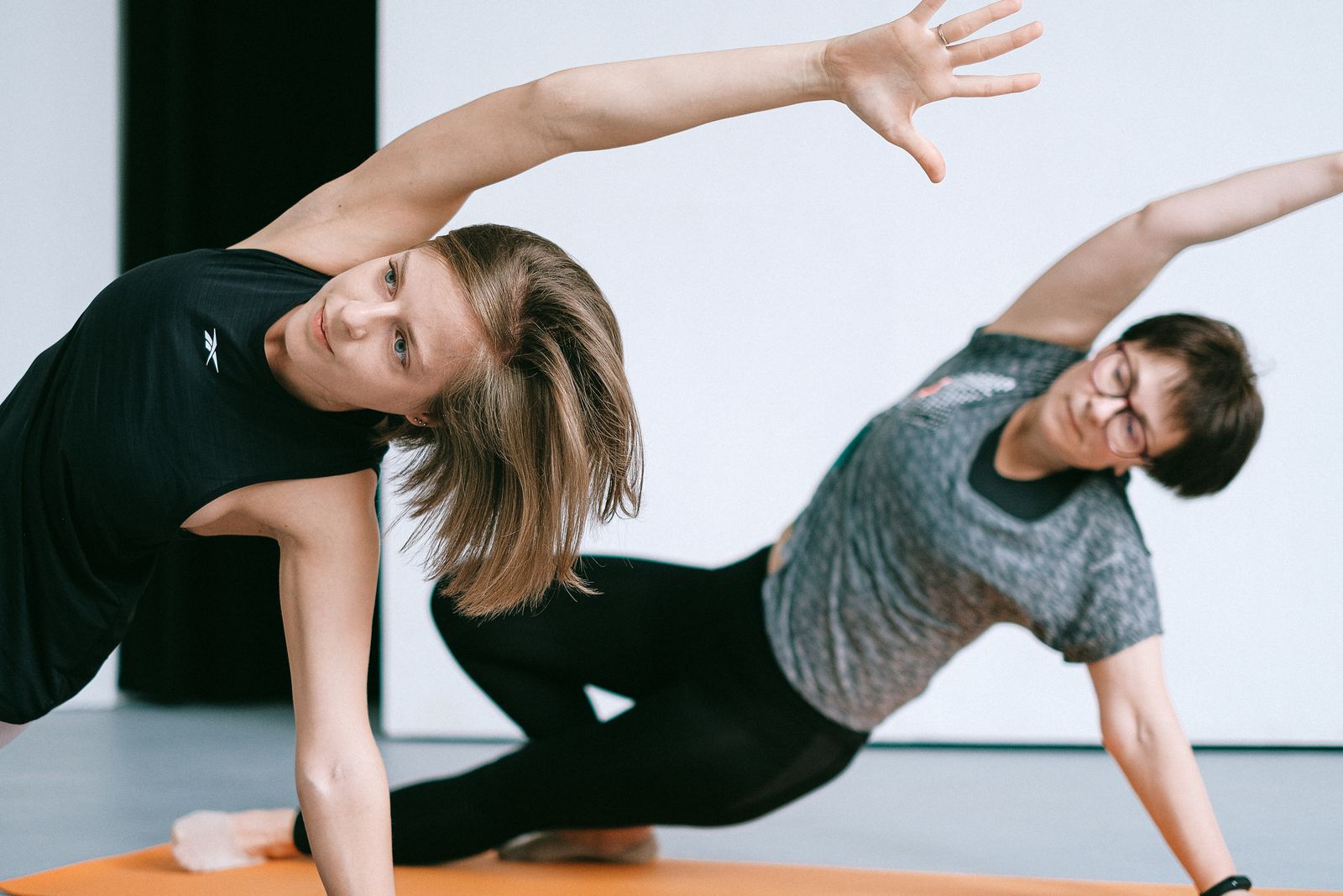 Two women doing yoga poses together on a studio mat.