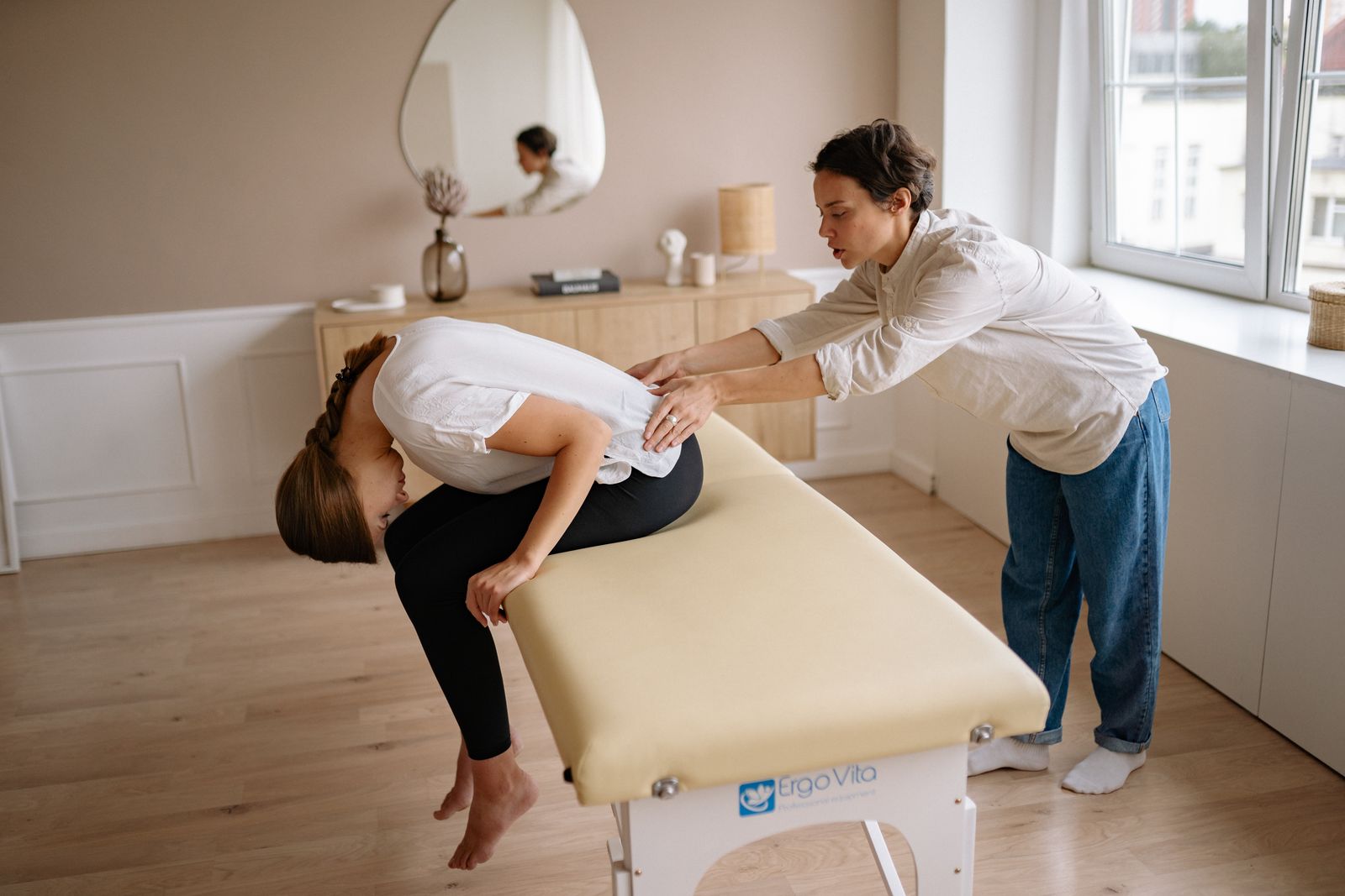A therapist applying pressure to a client’s lower back while the client bends forward on a treatment table.
