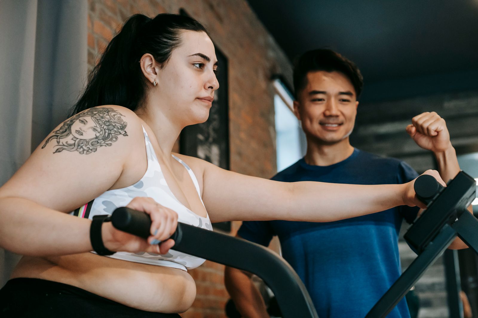 A trainer guiding a woman on an elliptical machine in a gym.