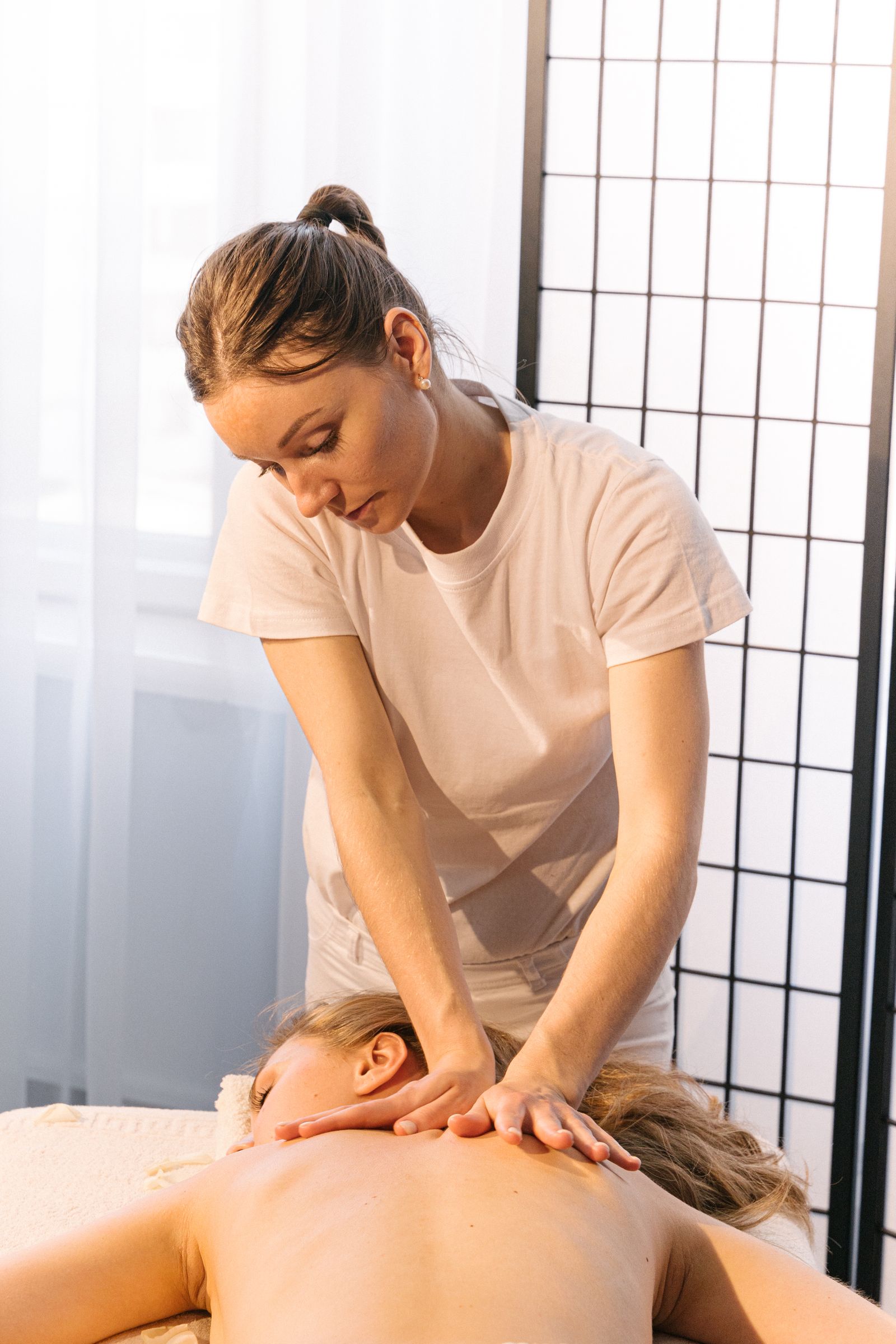 A massage therapist treating a client’s back in a spa room.